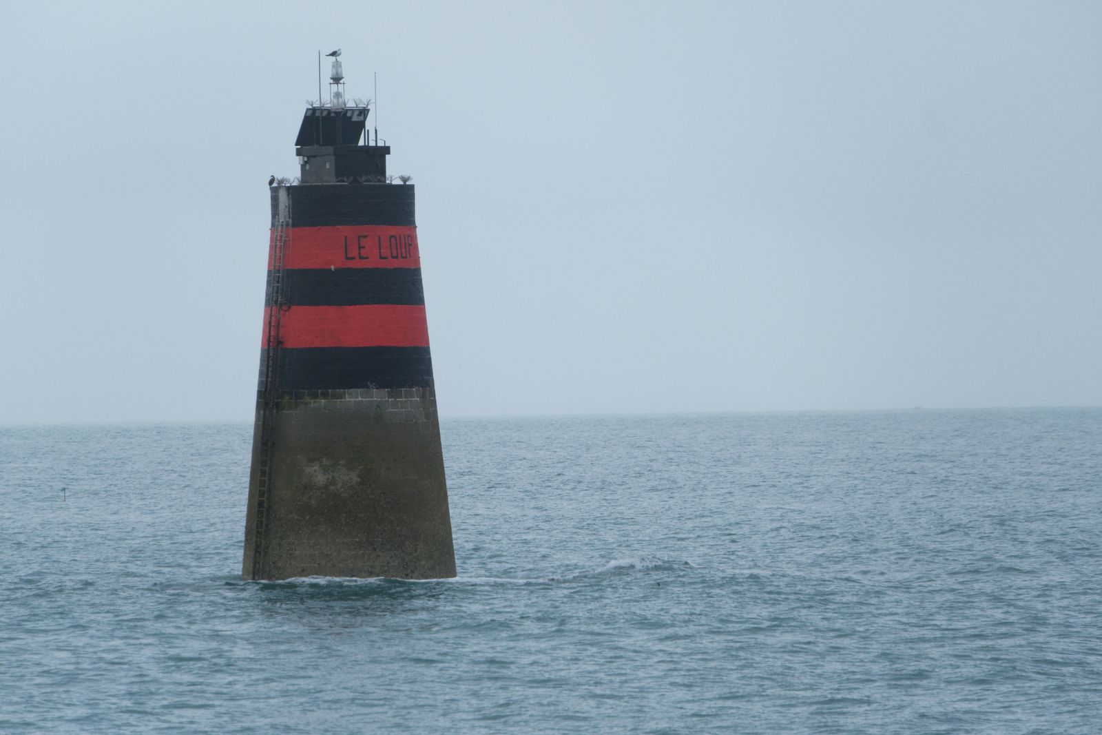 Solitary lighthouse 'Le Loup' standing in misty sea, France