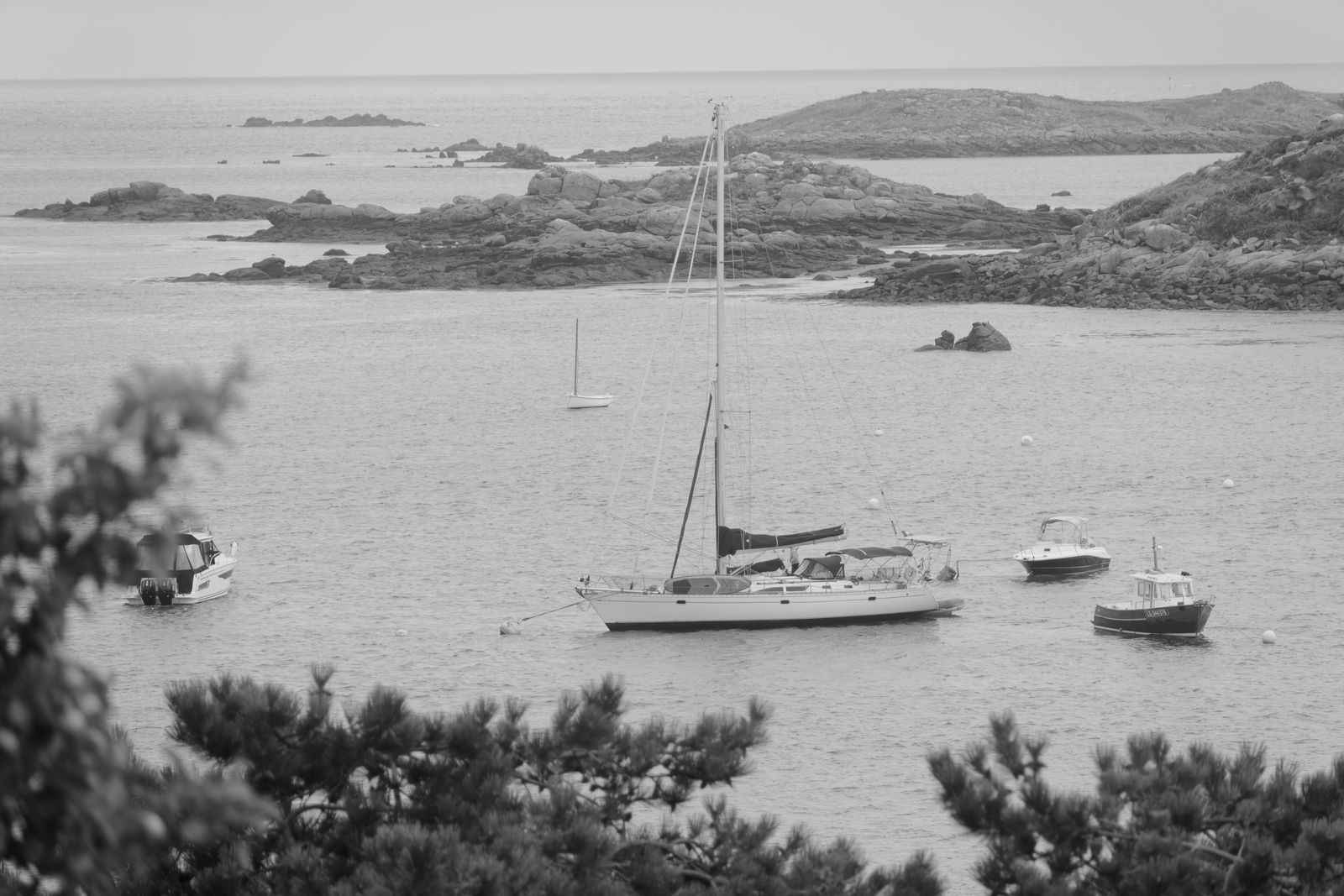 Vue en noir et blanc de voiliers au mouillage parmi les îlots rocheux de Chausey