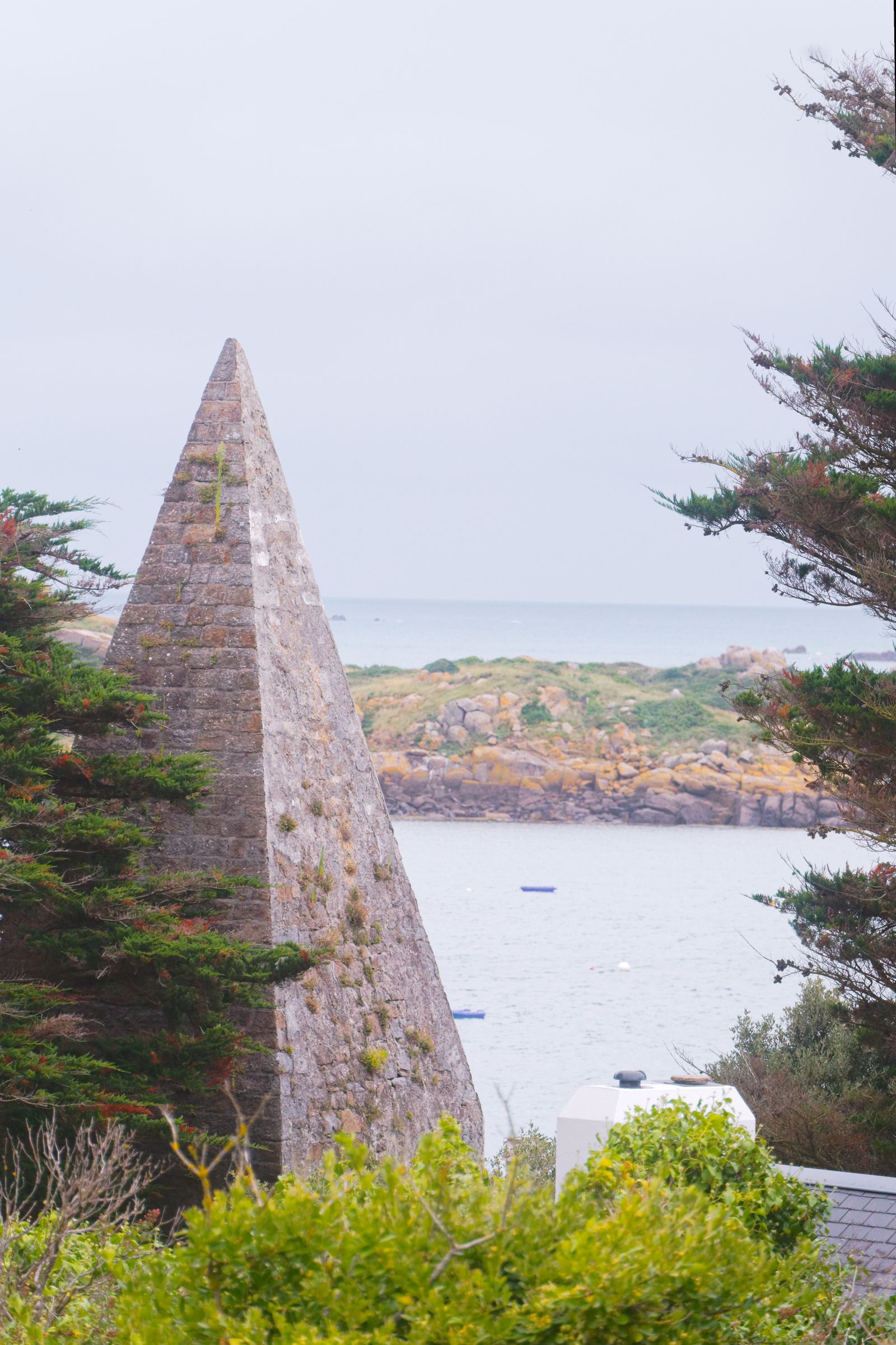 Coastal view of a stone pyramidal landmark surrounded by lush greenery in Chausey, France