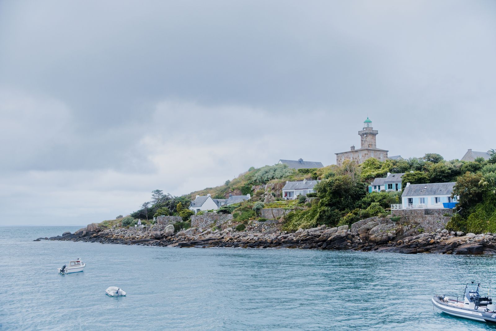 A picturesque lighthouse on the rocky coast of Granville, France, under a cloudy sky
