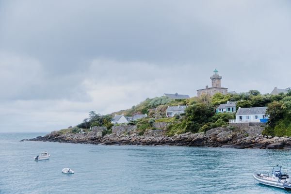 A picturesque lighthouse on the rocky coast of Granville, France, under a cloudy sky