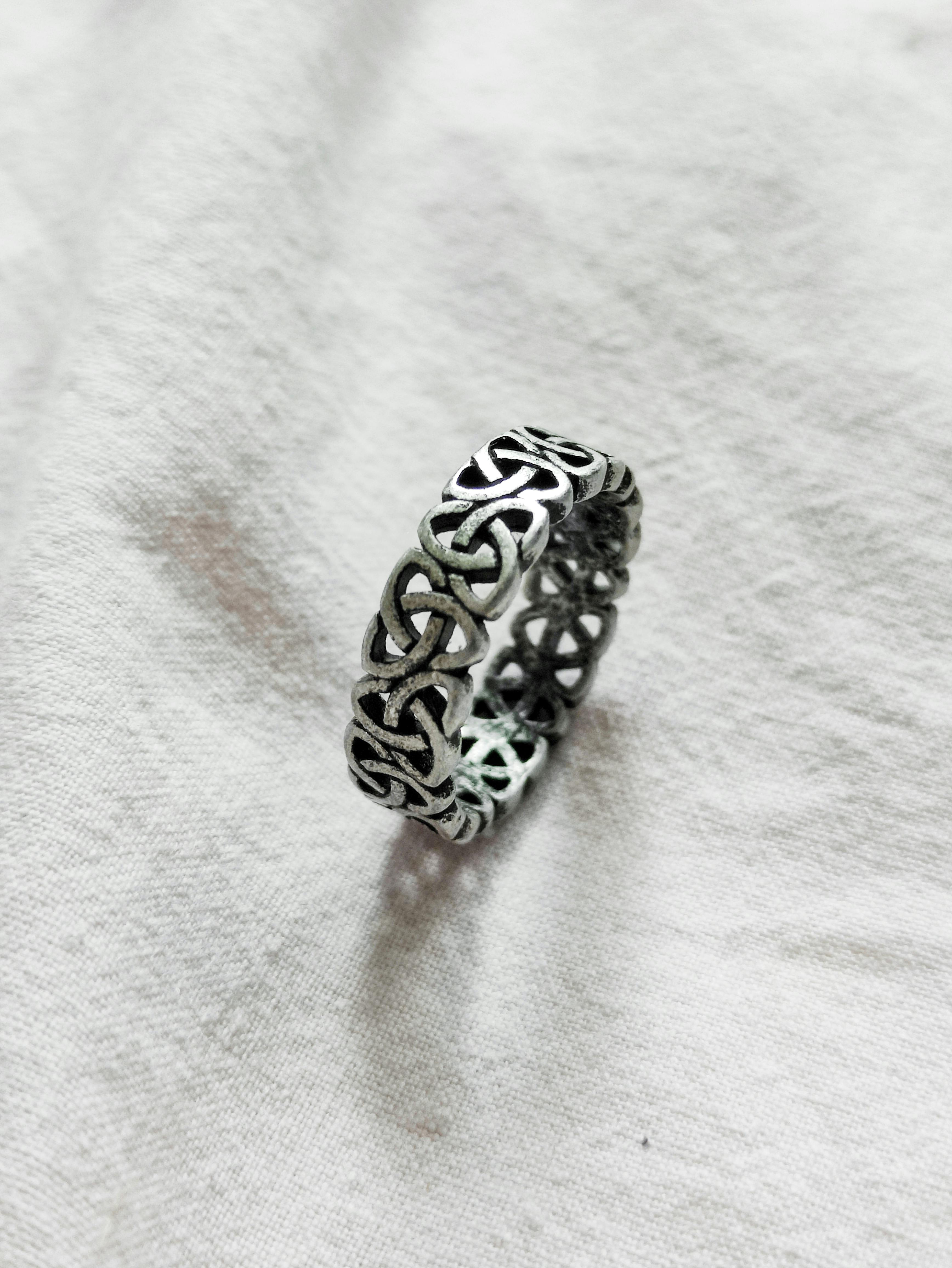 Elegant silver Celtic knot ring displayed on a textured white fabric background.