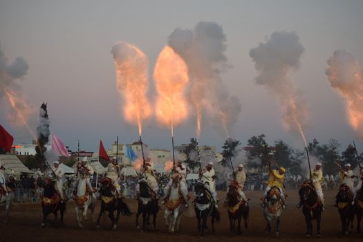Captivating scene of Moroccan horsemen in traditional attire firing rifles.