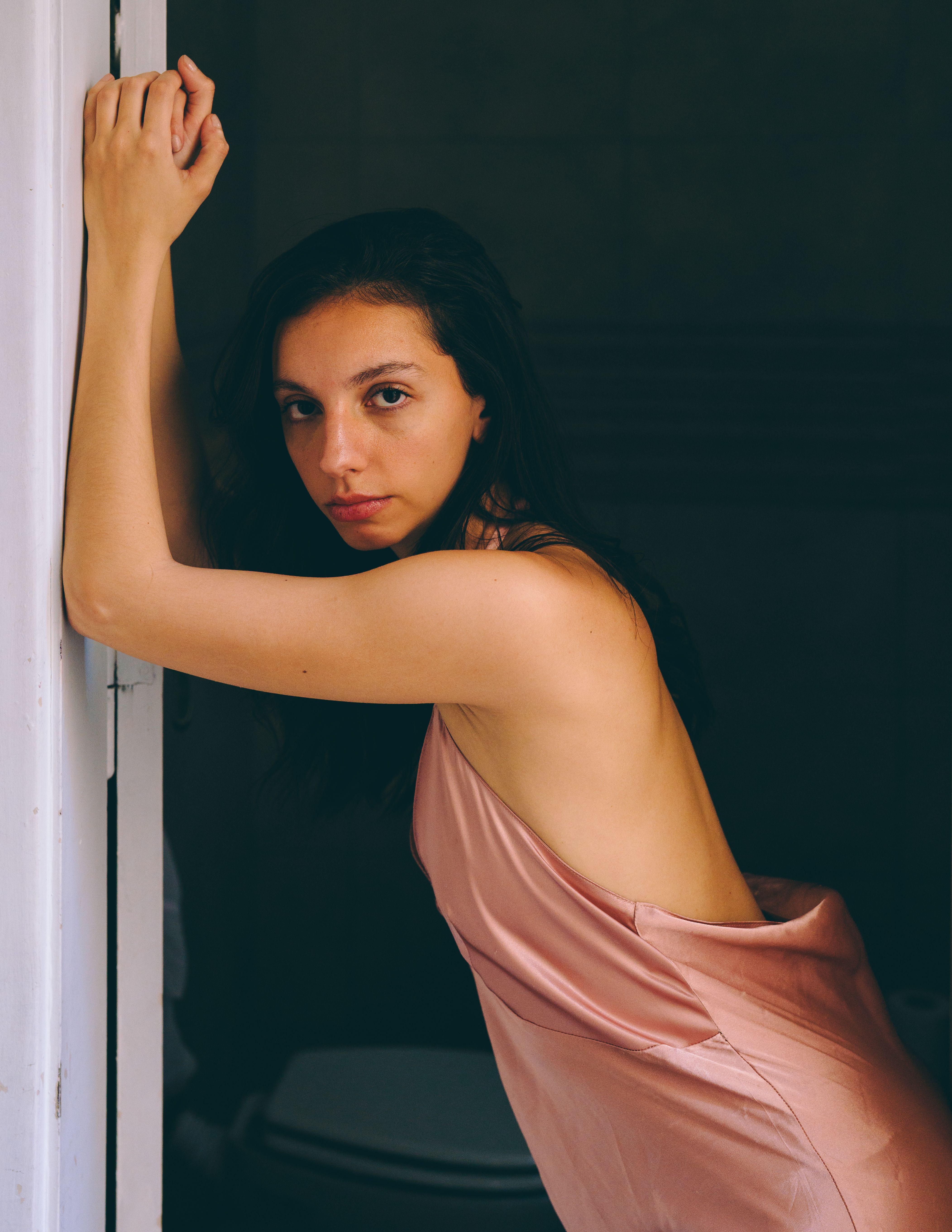 An elegant portrait of a woman in a pink dress leaning against a doorframe indoors.