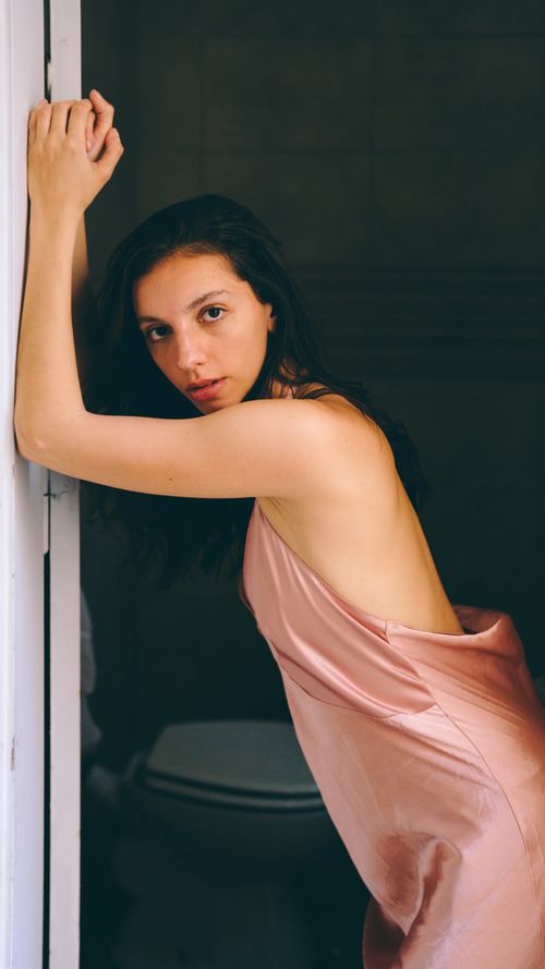 Free Young woman in a pink dress, thoughtfully leaning on a door frame indoors. Stock Photo