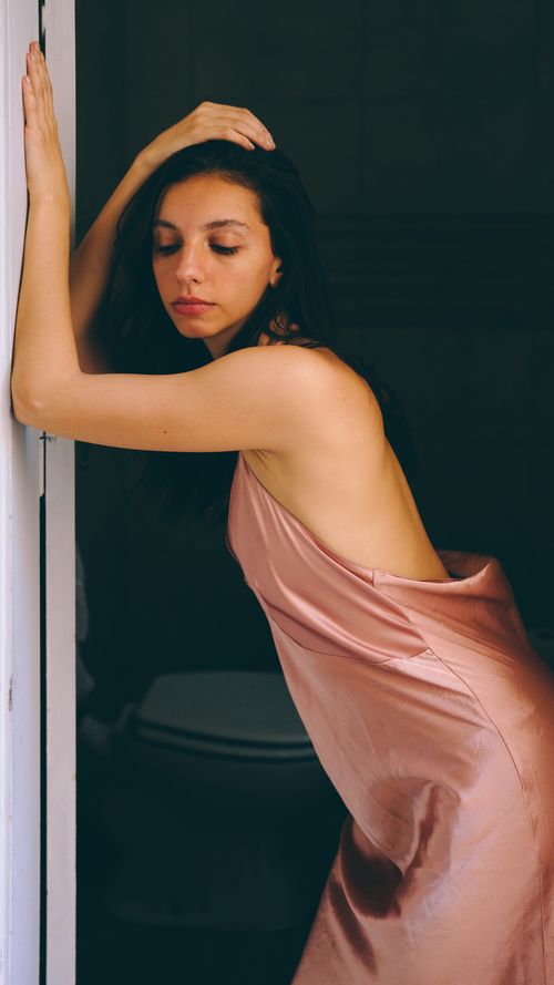 Free Woman in a soft pink satin dress leaning on a door frame, captured indoors. Stock Photo