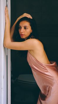 Portrait of an elegant woman in a pink satin dress leaning gracefully on a doorway, indoors.