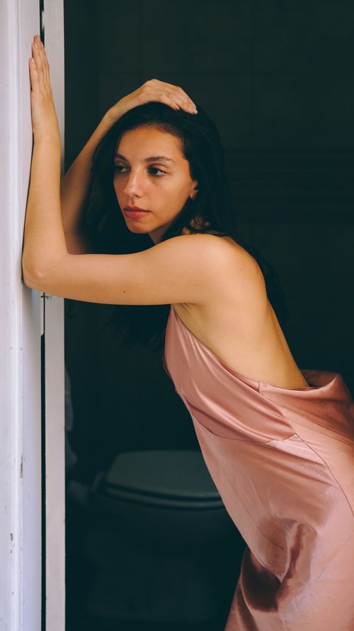 Free Portrait of an elegant woman in a pink satin dress leaning gracefully on a doorway, indoors. Stock Photo