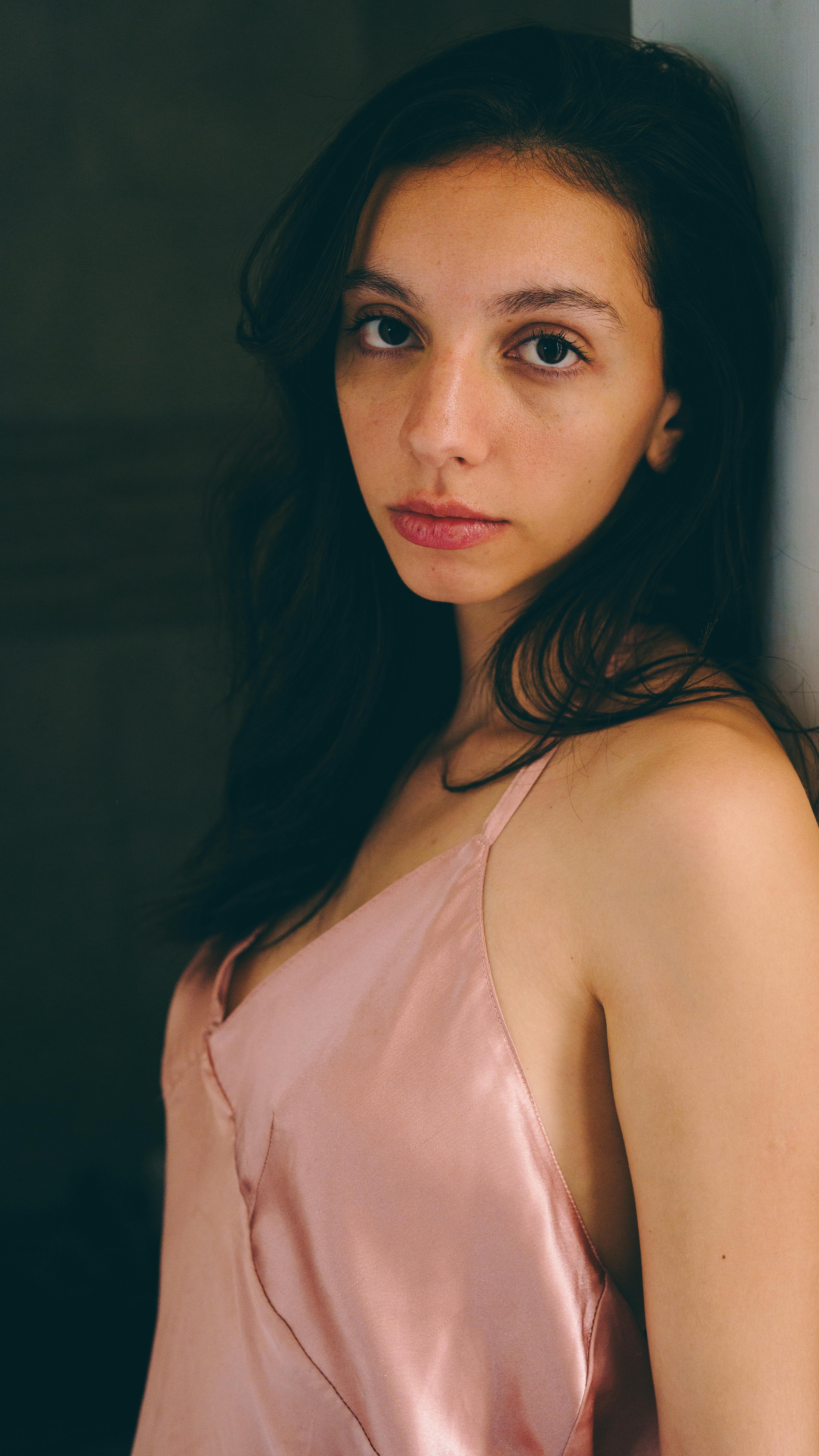 Portrait of a young woman in a pink silk top indoors, softly lit and relaxed expression.