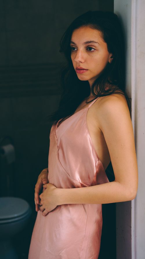 Free A young woman in a pink satin dress stands thoughtfully by a doorway. Stock Photo