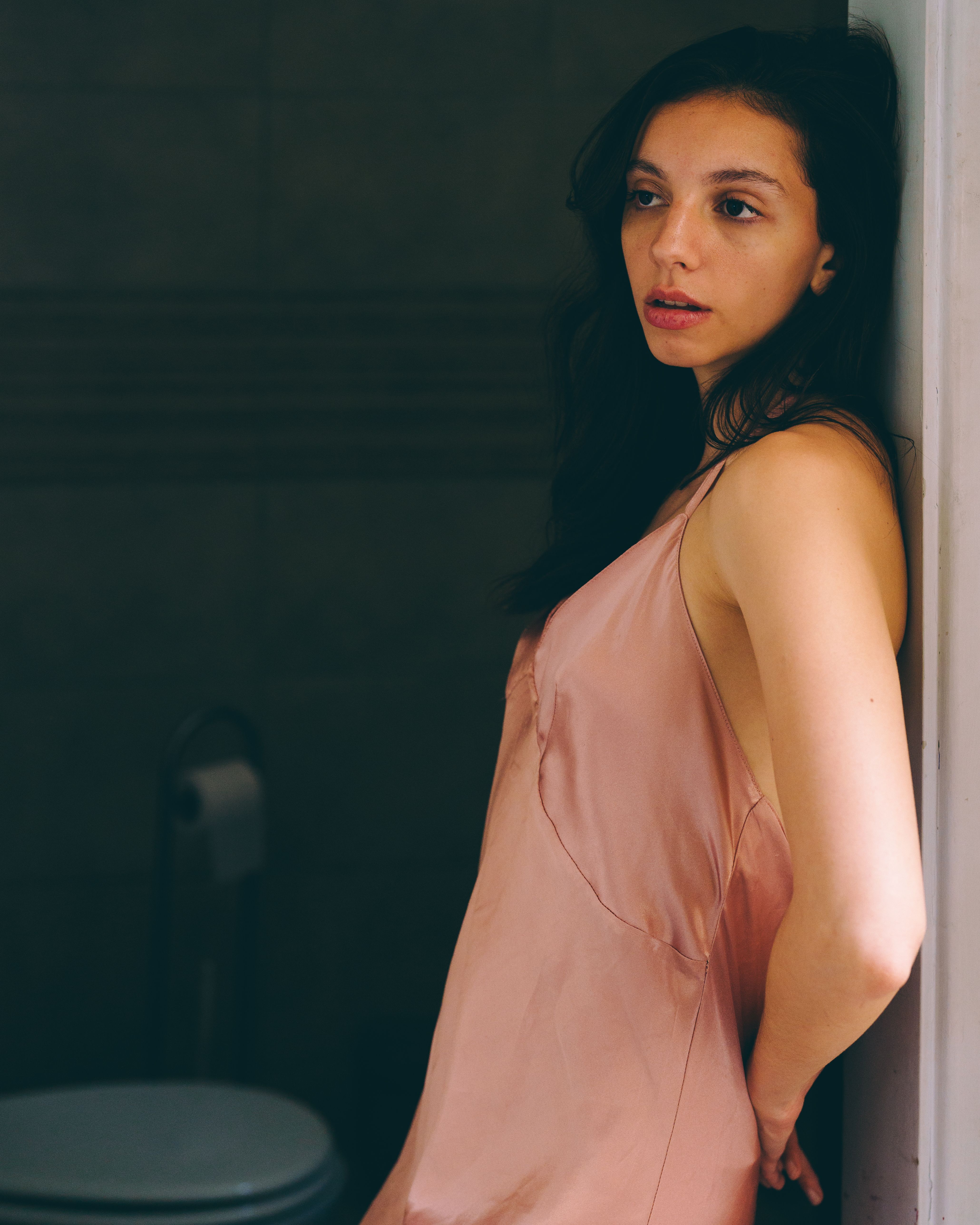 Artistic portrait of a woman in a pink dress leaning against a wall indoors.