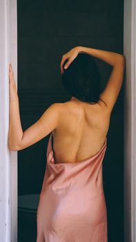 Woman in silky pink dress poses gracefully from behind, exuding elegance and beauty.
