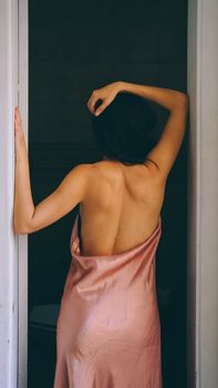 Back view of a woman wrapped in a silk dress standing inside a doorway.