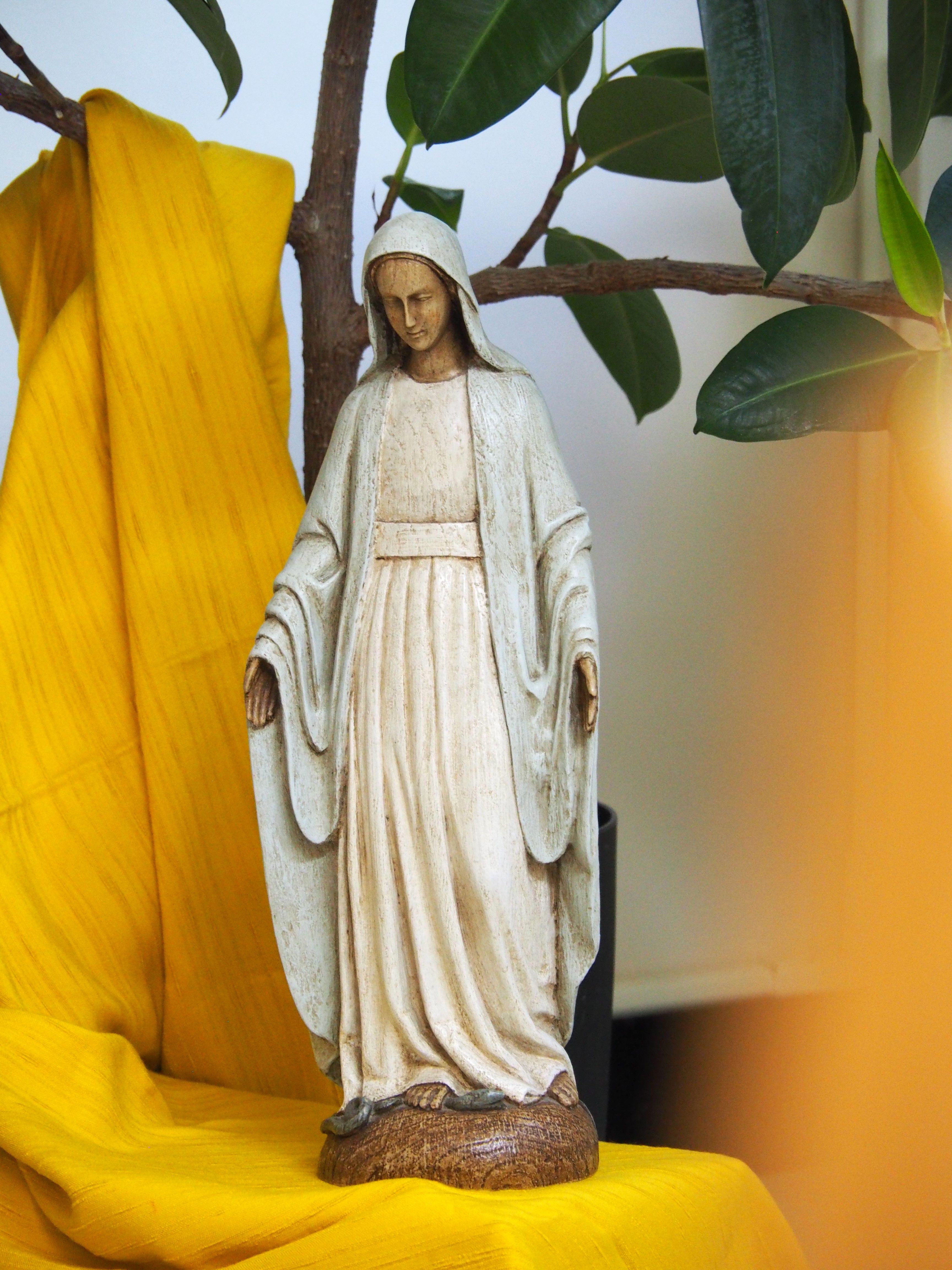 A detailed statue of the Virgin Mary surrounded by greenery and yellow drapery.