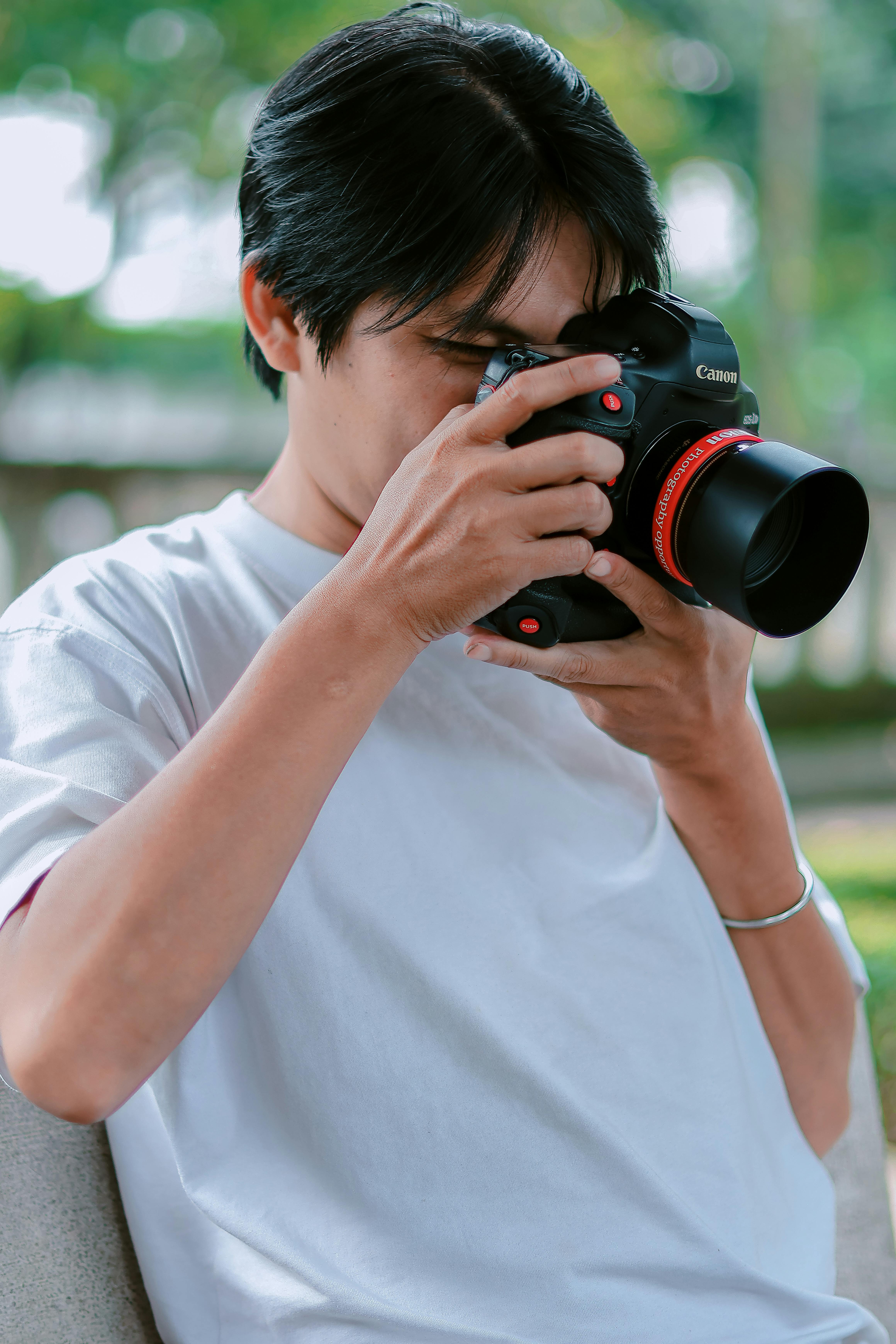 Free A young man with a camera focuses on capturing an outdoor scene. Stock Photo