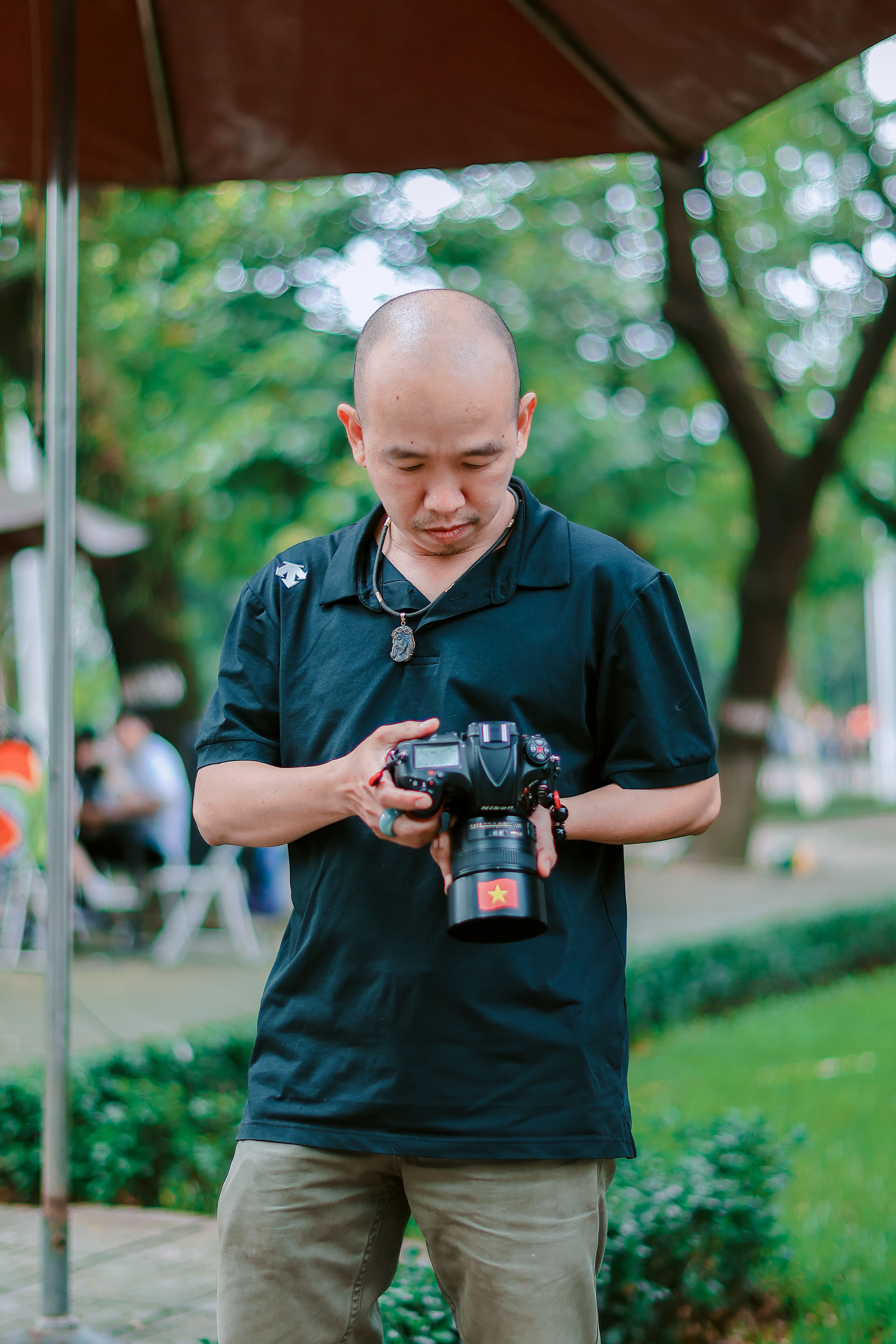 A male photographer examines his DSLR camera outdoors in a park area.