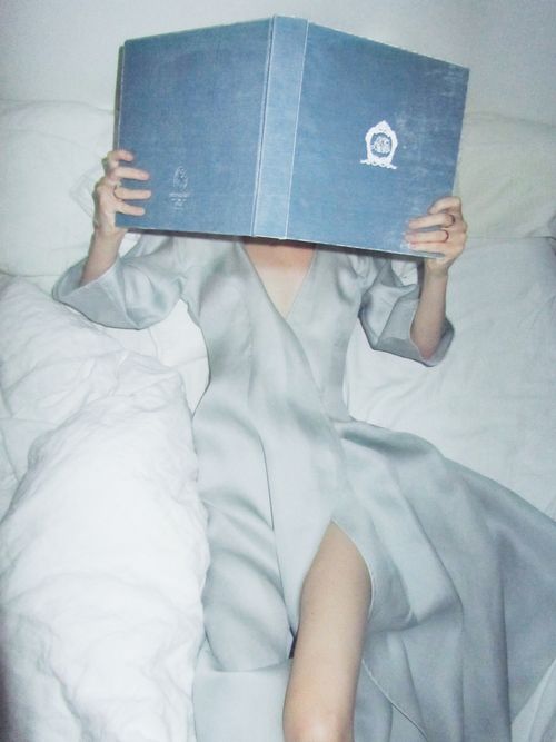 Free Adult woman relaxing in bed, reading a book with a serene expression and soft lighting. Stock Photo
