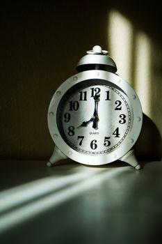 Classic vintage alarm clock casting shadow in sunlight indoors.