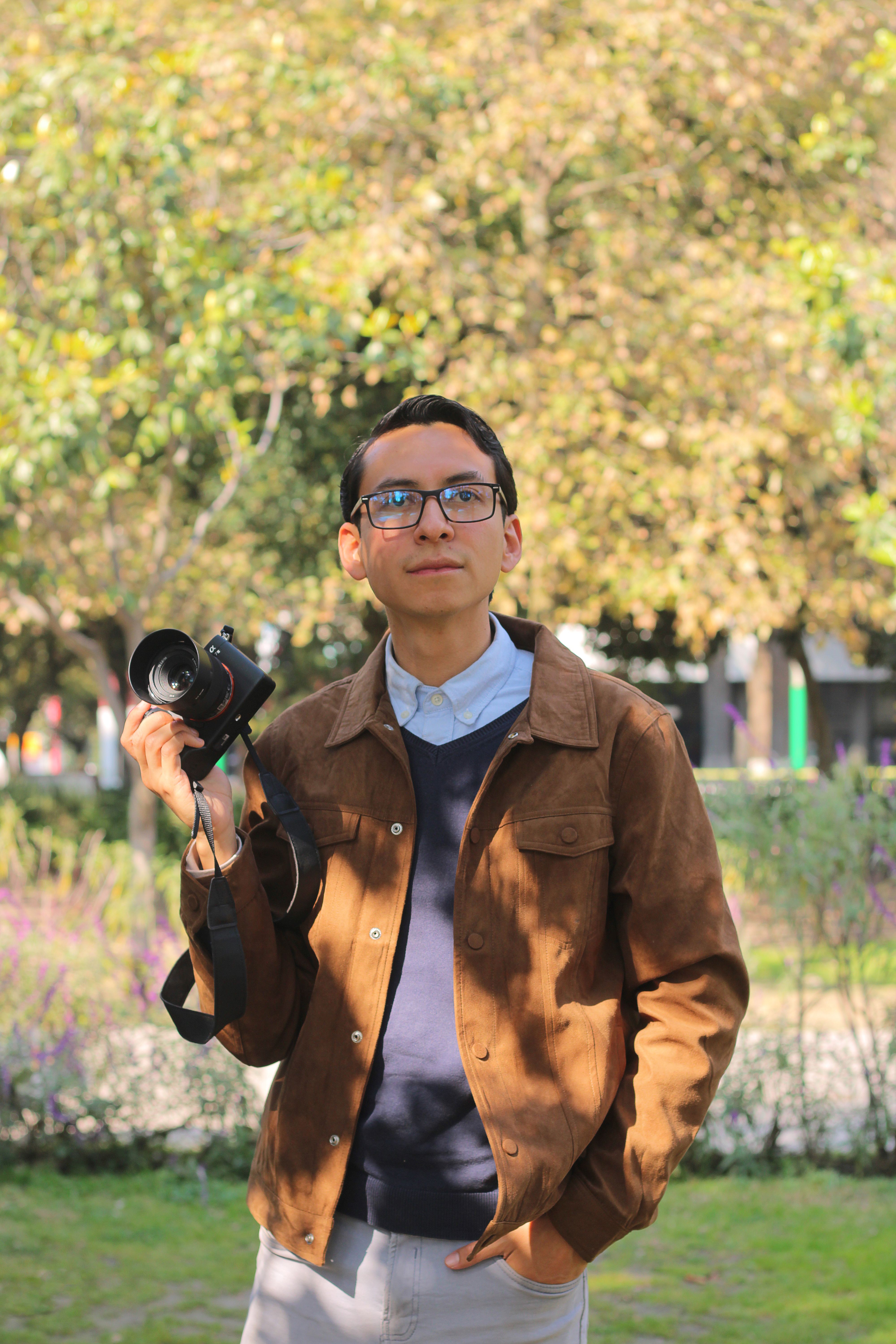 Young man with camera outdoors in a sunny park, ready for photography.