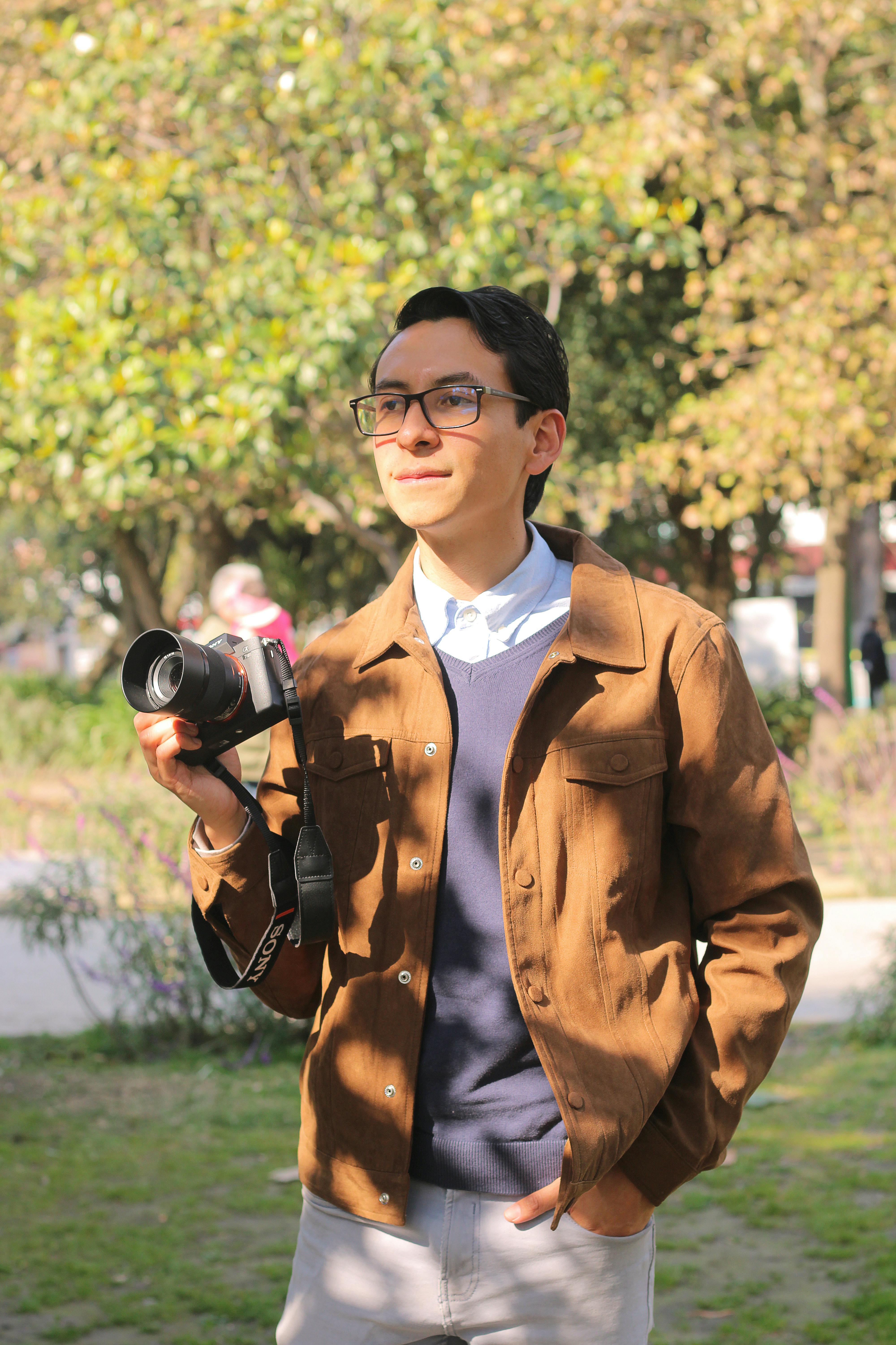 Young man holding a camera, standing outdoors on a sunny day, ready to capture moments.