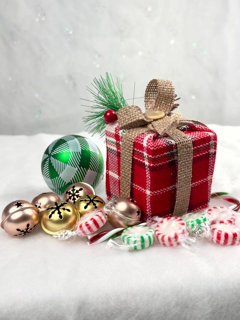 Red plaid gift with bells and candies on white background, capturing holiday spirit.