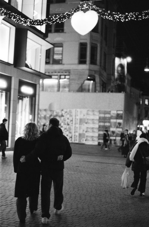 Free Couple walking arm in arm under heart decoration in Copenhagen street at night. Stock Photo