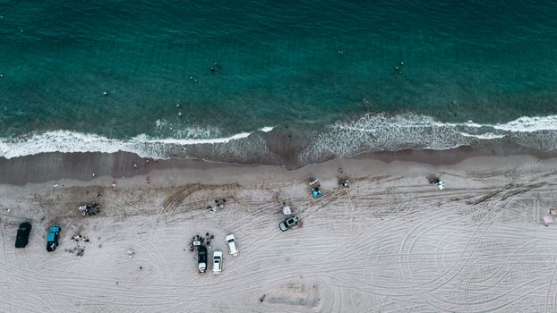 A stunning aerial view of Fujairah beach with cars parked along the shoreline and people enjoying the ocean waves.