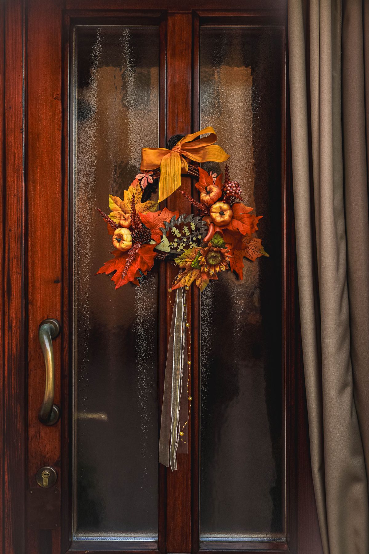 Decorative fall wreath on a glass door with warm light behind it
