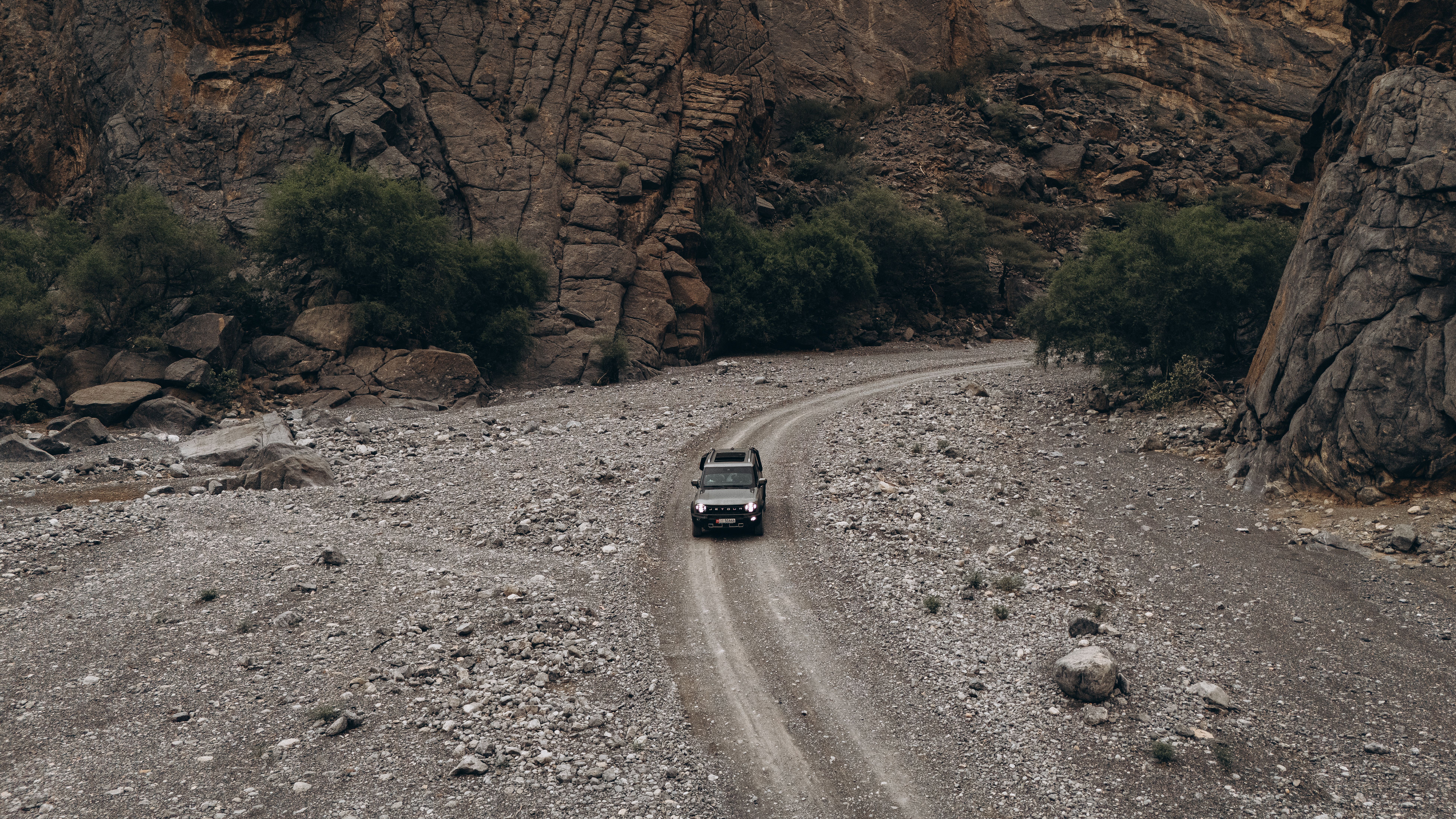 SUV driving through rough, rocky terrain in Oman's mountainous landscape, captured from above.