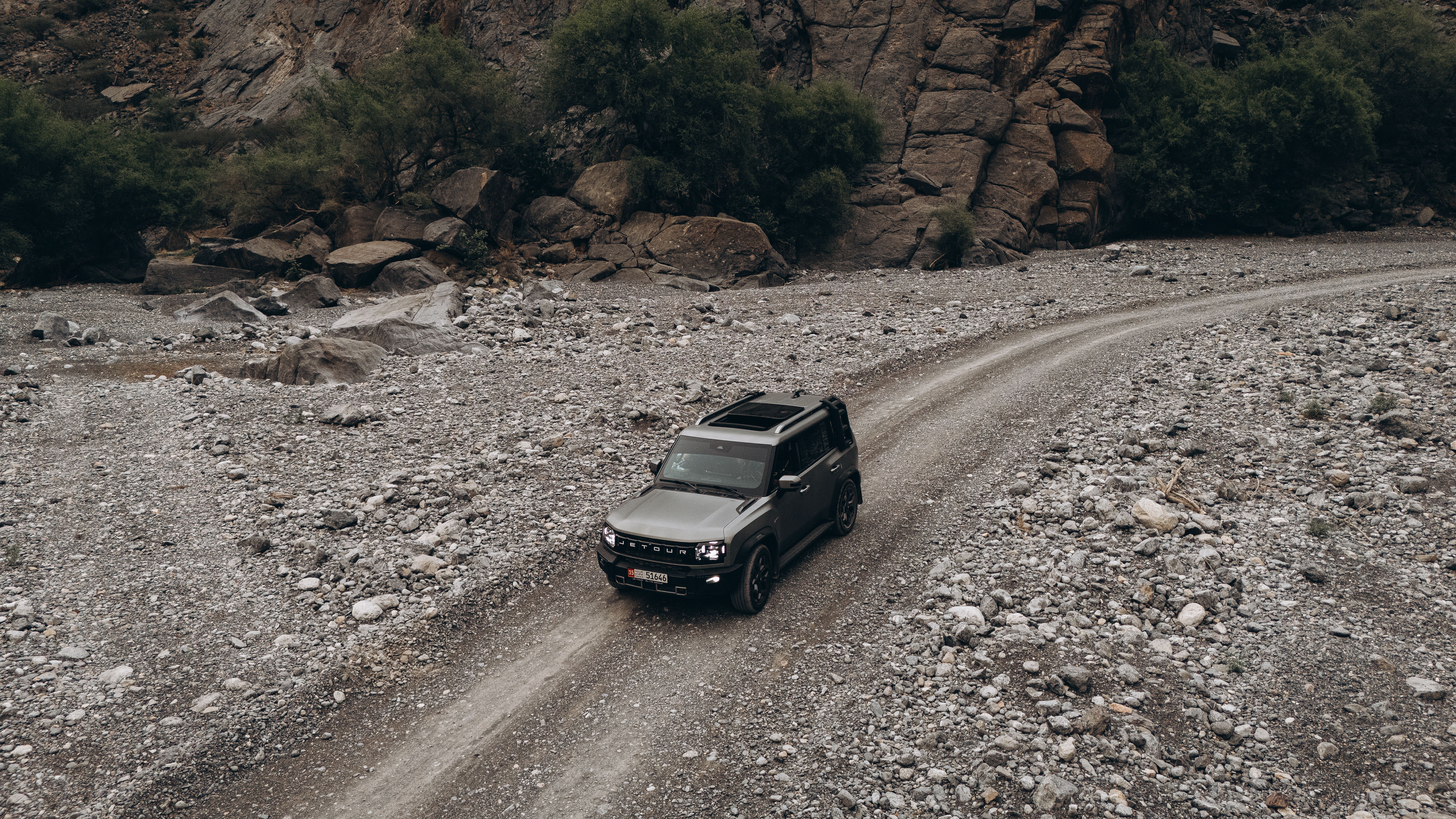 Aerial view of an SUV navigating a rugged, rocky path in the scenic landscapes of Oman.