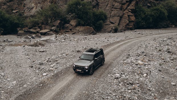 Aerial view of an SUV navigating a rugged, rocky path in the scenic landscapes of Oman.