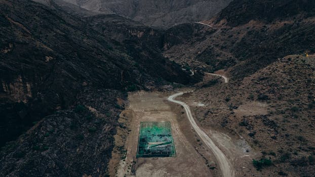 Drone shot of a rugged mountainous terrain with a football field nestled between peaks in Oman.