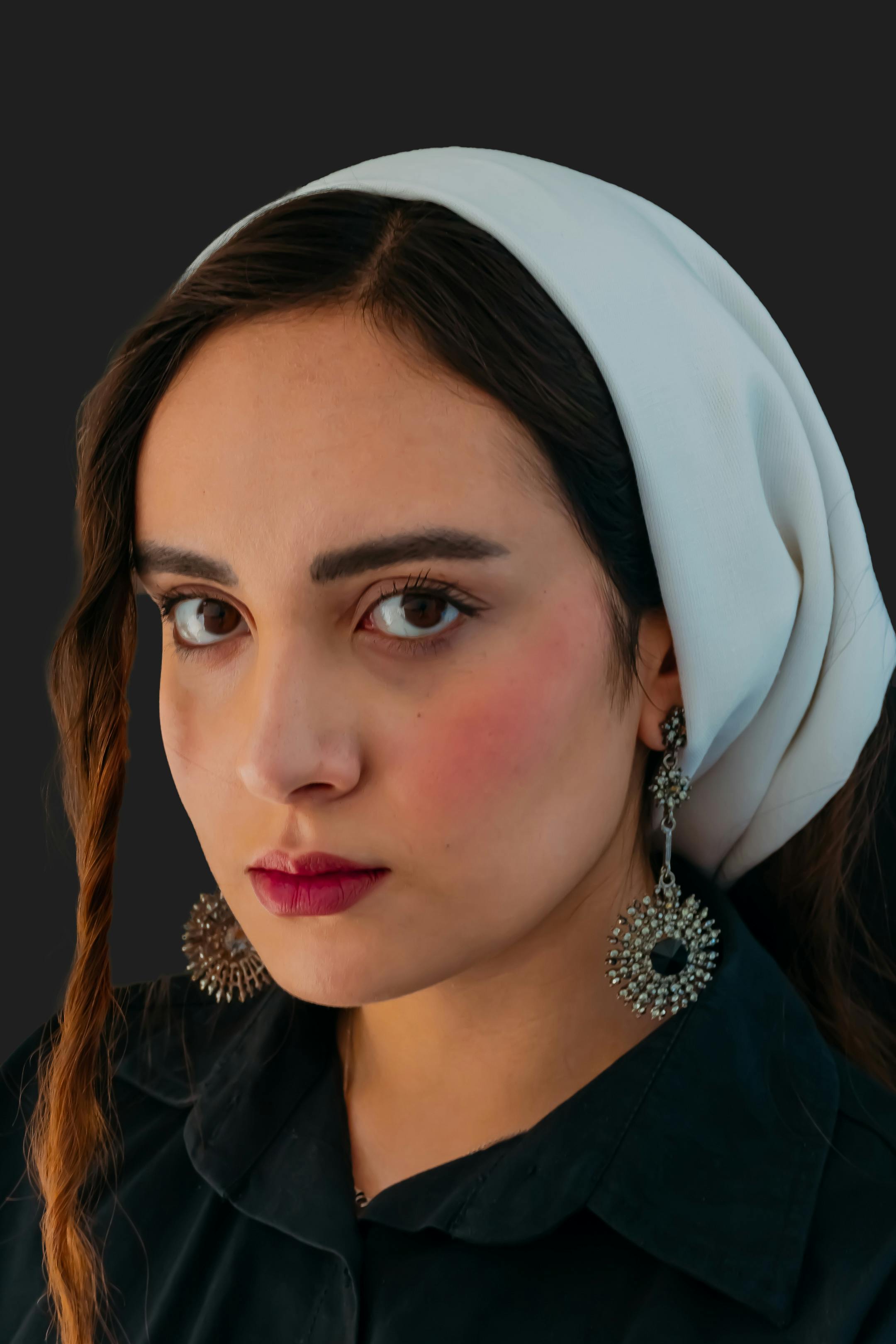 Zadarmo Detailný portrét ženy s bielou šatkou na hlave a výraznými náušnicami na tmavom pozadí. Fotka z fotobanky