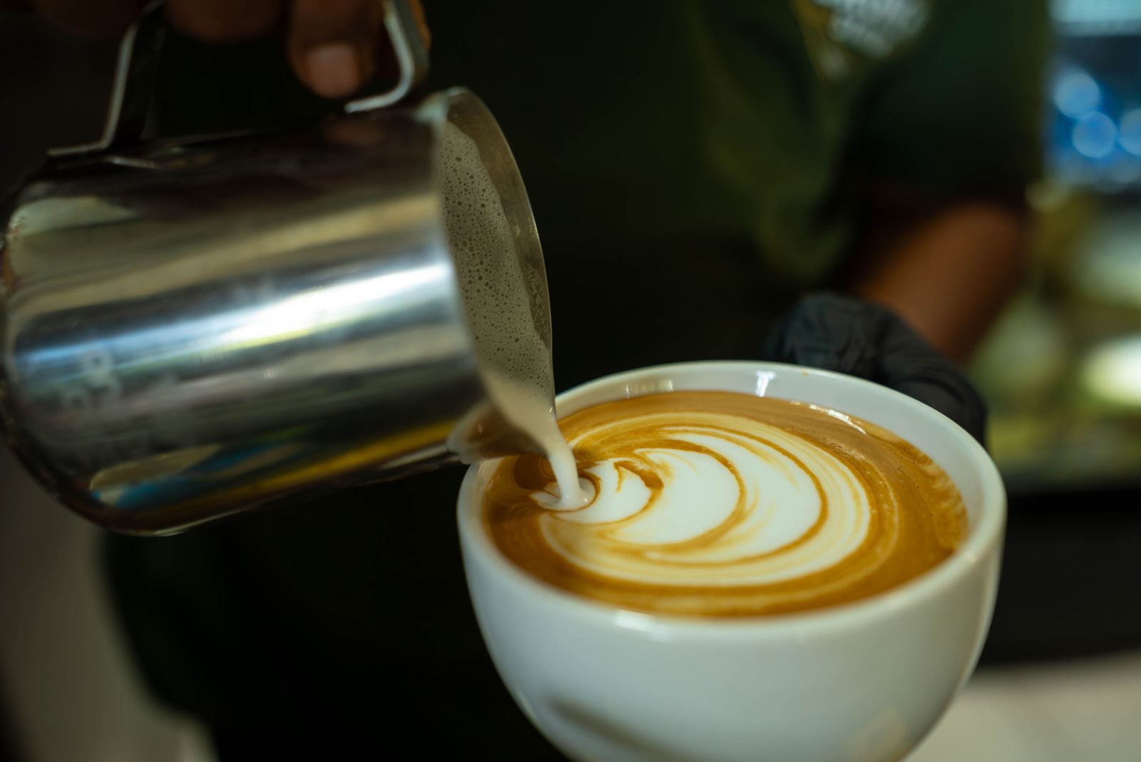 Unbranded stainless-steel milk pitcher pouring milk close to the coffee surface