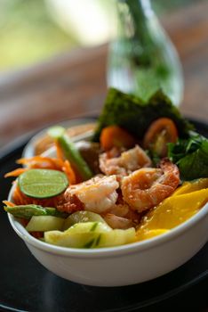 Colorful poke bowl featuring shrimp, fresh vegetables, mango, and lime for a refreshing meal.