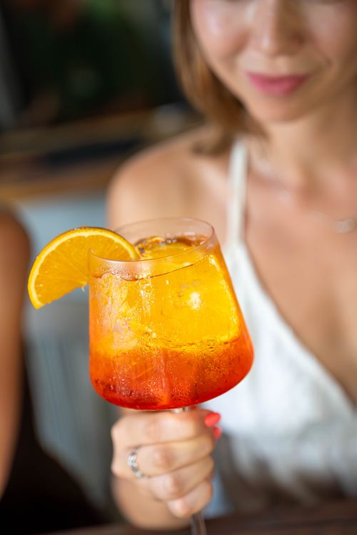 Free Close-up of Aperol Spritz cocktail with orange slice, held by woman in white dress. Stock Photo