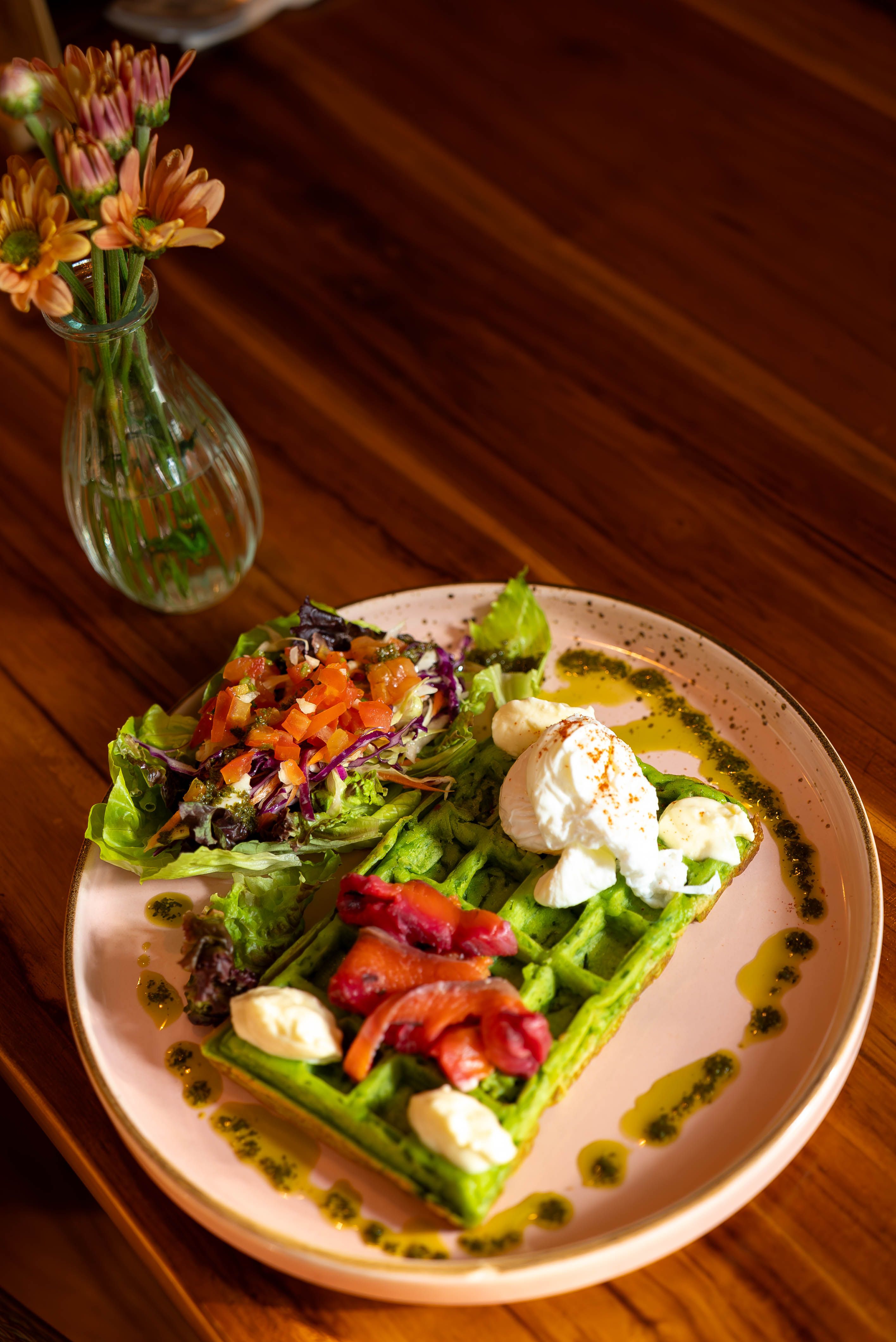 Delicious green waffles topped with creamy cheese, paired with fresh salad. Perfect for a gourmet breakfast.