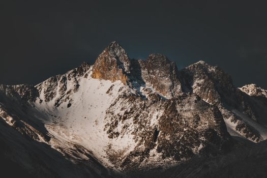 Breathtaking snow-covered mountain peaks under an ominous dark sky, captured in dramatic lighting.