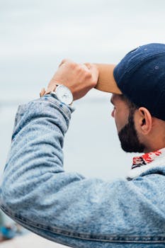 一名穿着休闲牛仔装的年轻人在户外调整帽子，手上戴着时尚手表