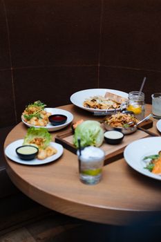 Gourmet meal setting on a round wooden table with various plates and drinks.