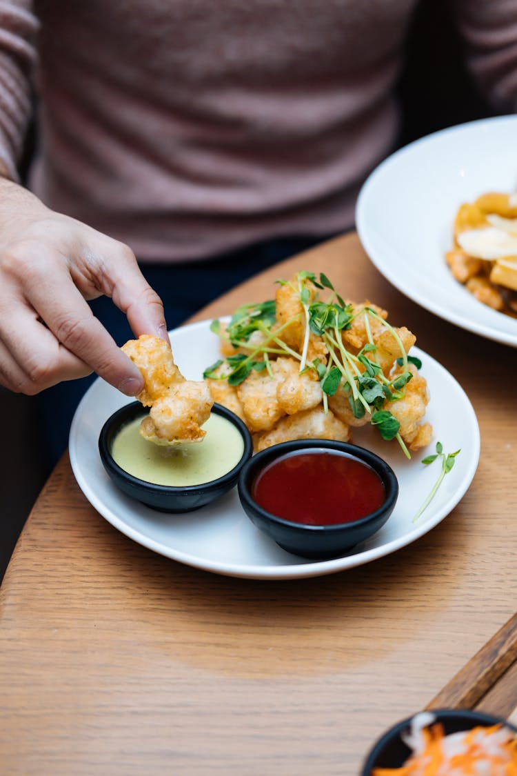 Person Dipping Fried Food On Sauce