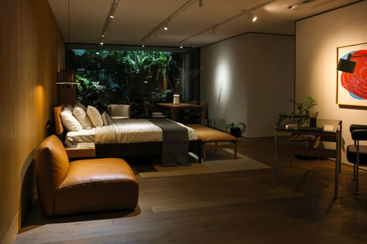 Elegant modern bedroom with plant decor, warm lighting, leather chair, and art in South Jakarta.