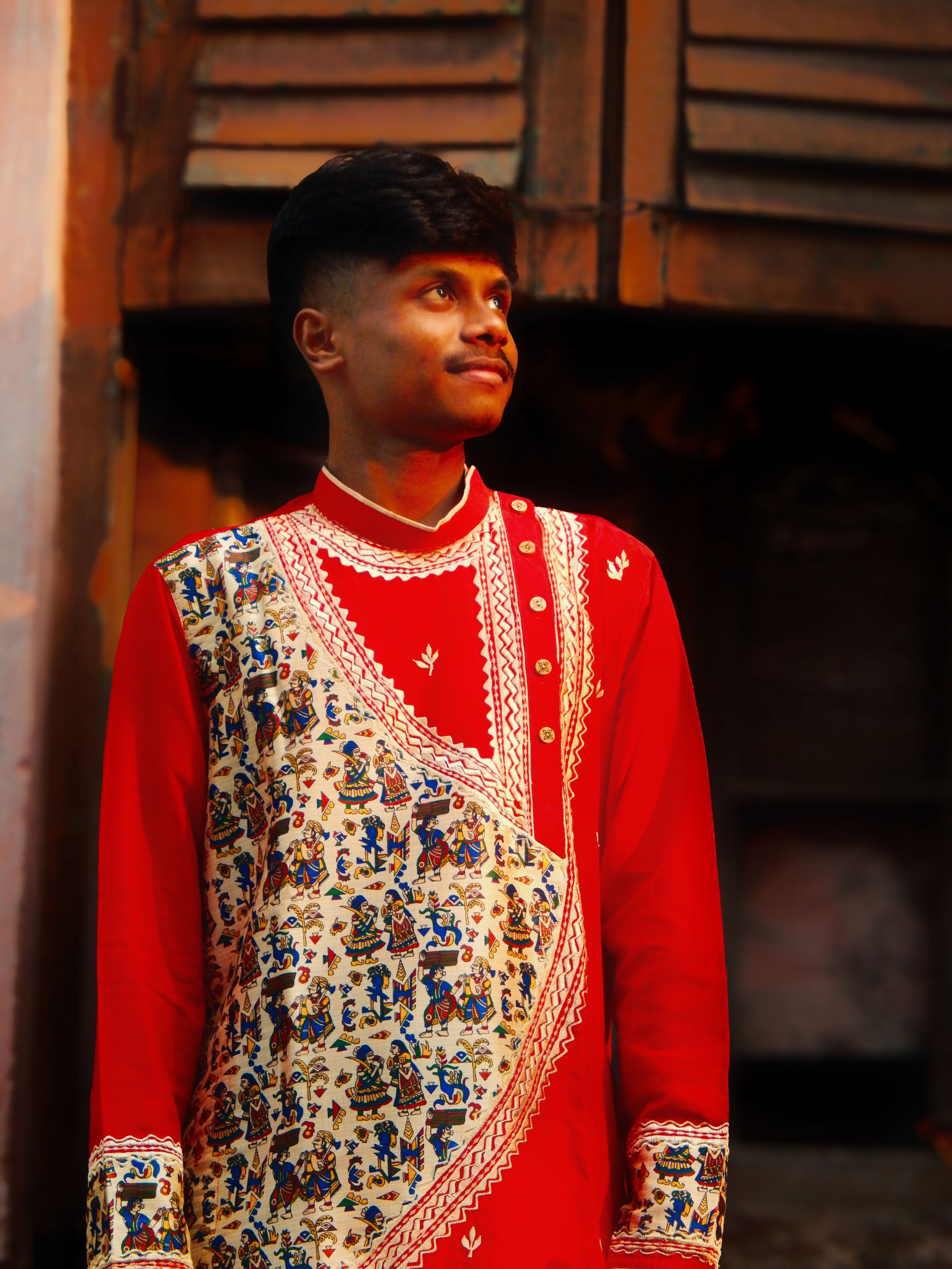 Portrait of a young man in vibrant traditional Indian clothing, outdoors in warm light.