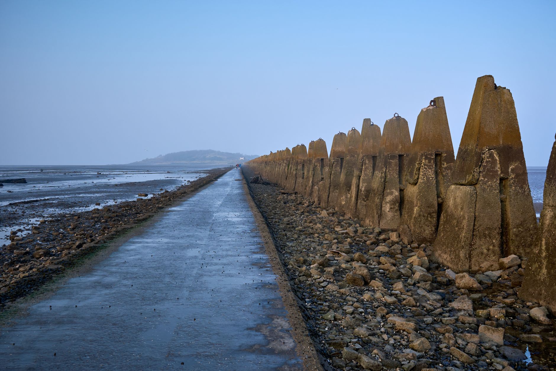 Tranquil view of Cramond Island path and sea defenses under a clear blue sky.