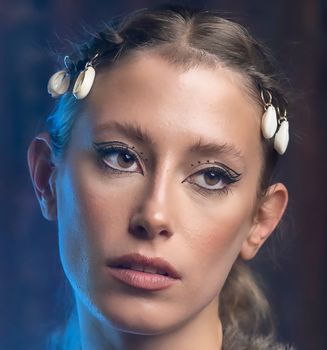 A woman with artistic makeup and shell hair clips, gazing thoughtfully. Captured in soft lighting.