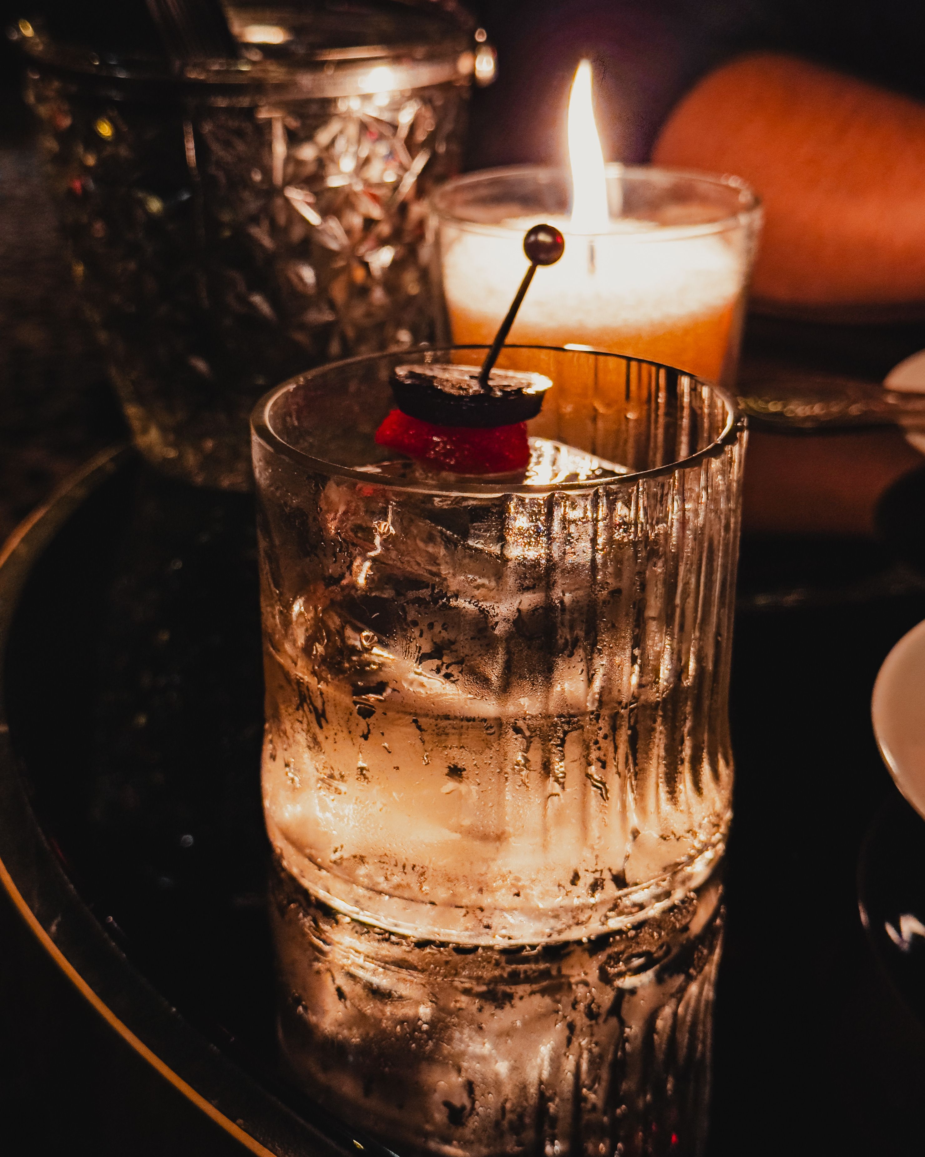 Close-up of a cocktail glass with cherry garnish in warm candlelight ambiance.