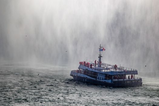 A sightseeing boat navigates close to Niagara Falls surrounded by mist.