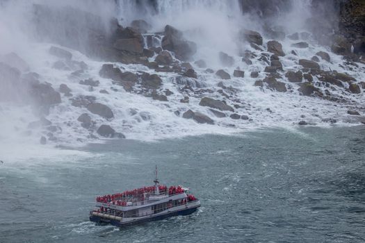 A tour boat filled with visitors in red ponchos approaches the base of a majestic waterfall at Niagara Falls.