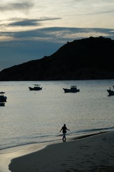 Serene beachfront at twilight with silhouette of person and boats.