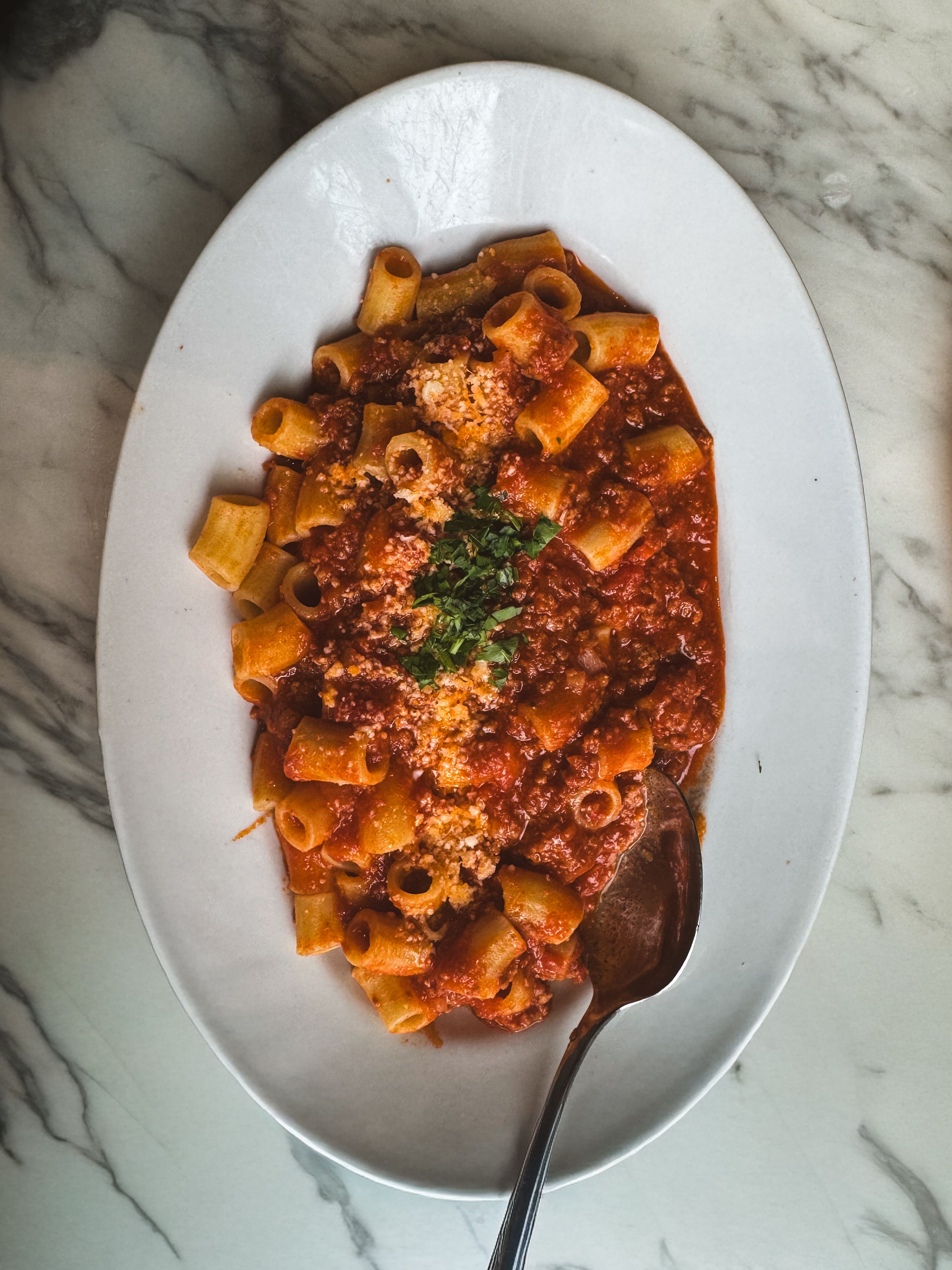 Fresh rigatoni pasta with rich tomato sauce and herbs on a white plate, perfect for a cozy meal.
